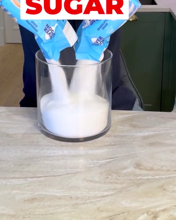 A large glass jar of white sugar on a kitchen counter beside a tub of Cadbury Drinking Chocolate